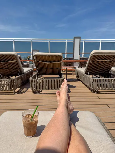 Güneşli bir günde okyanusa bakan bir yolcu gemisinde şezlongda oturan biri..