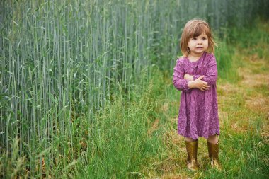 Charming child in dress and rubber boots near the wheat field in the rain