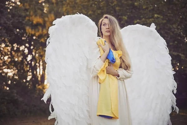 Beautiful girl dressed as an angel in the evening garden with Ukrainian flag
