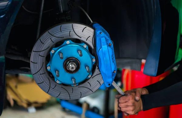 Car mechanic or serviceman disassembly and checking a disc brake and asbestos brake pads for fix and repair problem at car garage or repair shop