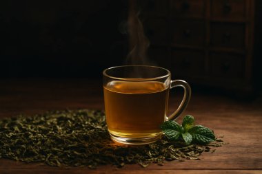 Yapay zeka, cam bardakta sıcak nane çayı buharda kurutulmuş bitkisel yapraklar ve ahşap masa üzerinde taze nane şekeri antika eczane arka planında yumuşak ışık ve sıcak ruh hali üretti.