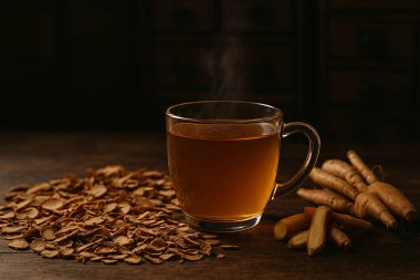 Yapay zeka cam bardaktaki bitki çayının görüntüsünü oluşturdu. Kurumuş ve taze parmak kökü ahşap masa üzerinde. Eski Çin eczacısının arka planında.