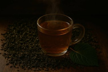 Yapay zeka, sade bardakta dut yaprağı çayını, kurumuş ve taze dut yapraklarıyla birlikte, yıllanmış aydınlatma altında, sade ahşap bir masada üretti.