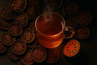 Kurutulmuş bael dilimleri ve ahşap masa üzerinde sıcak vintage ışık ile taze meyve ile çevrili cam fincanda bael meyve çayı üst görünümü oluşturdu.