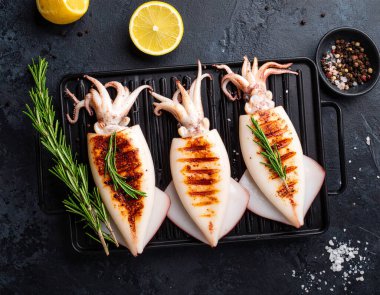 Yapay zeka kömürün üzerinde ızgara yapılmış taze mürekkep balığının üst görüntüsünü oluşturdu. Yumuşak dokular ve aromatik dumanla mükemmel pişirildi. Tuz ve karabiber ile tatlandırılmış, biberiye filizi ile süslenmiş.