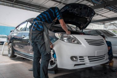 Araba tamircisi ya da tamirci tamirhanedeki ya da tamirhanedeki tamir ve onarım problemleri için kaporta ve fiber tampon parçalarını kontrol edip onarıyor.