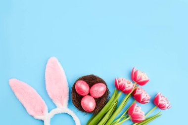 Mutlu Paskalya tebrik kartları. Yuvada pembe paskalya yumurtaları, bir buket lale ve mavi arka planda tavşan kulakları. Uzayı kopyala Üst görünüm.
