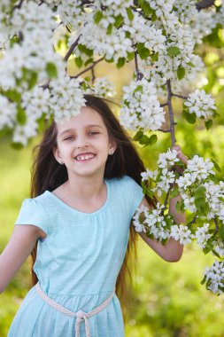 Çiçekli bir elma bahçesinde gülümseyen genç bir kız. Dikey yönelim