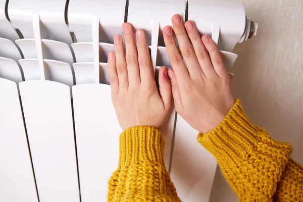 stock image A woman warms her hands on a heater. Cold temperature in the house. The concept of a cold winter, problems with central heating in the apartment. 