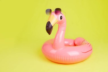 Sarı arka planda güneş gözlüklü şişme flamingo, plaj oyuncağı. Kopyalama alanı olan yaz arkaplanı. 