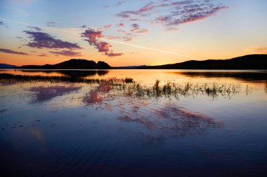 Baykal Gölü 'nde renkli bir gün doğumu. Bulutlar suyun yüzeyine yansıyor. Güneş, Olkhon adasının üzerinden dağların üzerinden doğuyor.