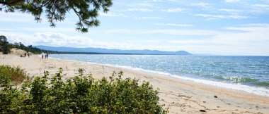 Güneşli bir yaz gününde güzel kumlu bir sahil. Turistler deniz kenarında dinlenir. Sancak..