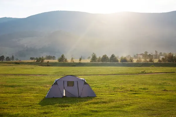 stock image A tent in a meadow near a mountain landscape in the rays of the setting sun. The concept of outdoor travel. 