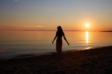 Güzel bir kız kumlu bir sahilde gün batımının tadını çıkarır. Yaz tatili, deniz tatili.. 