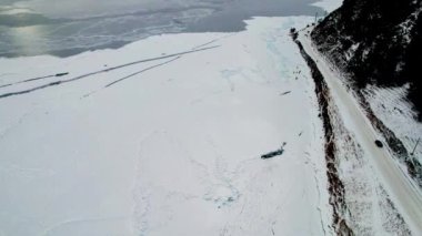 Yol, gölün karlı kıyısına ve resimli dağlara yakındır. Karlı bir havada donmuş göl. 