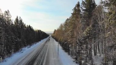 Arabalar karla kaplı bir ormanda uzun ve dolambaçlı bir yol boyunca yol alırlar. Havadan kış manzarası. 