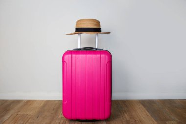 Pembe bavul ve hasır şapka bir otel odasında duvara dayanıyor. Yaz seyahati, yolculuk hazırlıkları..