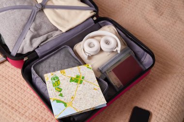 İçinde kıyafet, harita, kulaklık ve yolculuk için gerekli belgeler olan bavulu aç. Seyahat kavramı