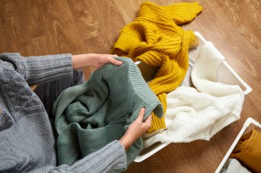 Genç bir kadın düzgün örülmüş giysileri metal bir çamaşır sepetine koyuyor. Düzeni sağlama, temizlik, dağınıklık, düzenleme....