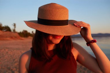 Gün batımında kumlu bir sahilde hasır şapkalı çekici bir kızın portresi..
