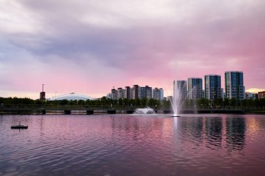 Günbatımı sakin bir göle yansıyor fıskiyesi ve arka planında şehir silüeti olan. 