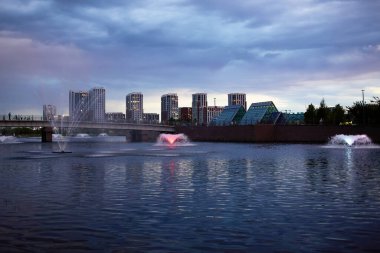 Akşam şehri manzarası. Günbatımında modern şehir binalarıyla çevrili sakin bir göl..