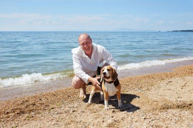 Sıcak bir yaz gününde deniz sahilinde av köpeğiyle rahatlayan gülümseyen bir adam..