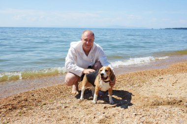 Sıcak bir yaz gününde deniz sahilinde av köpeğiyle rahatlayan mutlu bir adam..