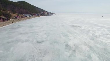 Baharda Baykal Gölü, Listvyanka Köyü. Turistli arabalar göl boyunca yol boyunca sürüyorlar ve hoverkraftlar buzun üzerinde sürüyorlar.. 