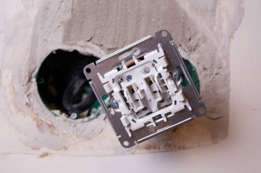 Duvara monte edilen bir elektrik prizinin yakın çekim görüntüsü. Arka plan kısmen korunmasız bir duvar gösteriyor, bu da yenileme çalışmalarını gösteriyor.. 