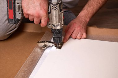 Mobilya menteşesi takmak, mobilya montajı ve montajı. Elektriksiz tornavida kullanarak kapı menteşesini mobilyaya vidalamak..