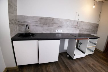 Modern bir apartman yenileme sırasında siyah lavabosu olan bir mutfakta modern tezgah ve beyaz dolap kurulumu.