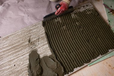 İşçi, gündüz saatlerinde inşaat alanında desenli bir yüzeye çimento sürüyor. Yerleşim alanına fayanslar döşenmiş.. 