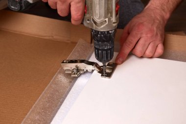 Mobilya menteşesi takmak, mobilya montajı ve montajı. Elektriksiz tornavida kullanarak kapı menteşesini mobilyaya vidalamak..