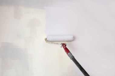 Bir kişi, yenilenmekte olan bir odada duvarın açık renkli bir kısmını kaplamak için boya silindiri kullanıyor. Doğal ışık içeri giriyor, işi güçlendiriyor.. 