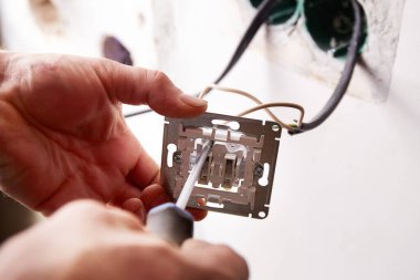 Bir işçi tornavida kullanarak duvara elektrik prizi takıyor. Daire tadilattan geçiyor..