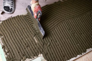 İşçi, gündüz saatlerinde inşaat alanında desenli bir yüzeye çimento sürüyor. Yerleşim alanına fayanslar döşenmiş.. 