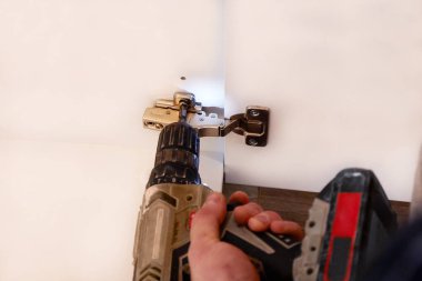 Elektriksiz tornavida kullanarak kapı menteşesini beyaz mutfak mobilyalarına vidalamak. Mobilya menteşesi takmak, mobilya montajı ve montajı.