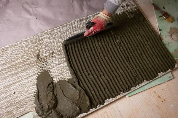 İşçi, gündüz saatlerinde inşaat alanında desenli bir yüzeye çimento sürüyor. Yerleşim alanına fayanslar döşenmiş.. 