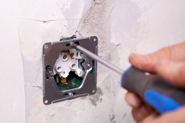 Bir işçi tornavida kullanarak duvara elektrik prizi takıyor. Daire tadilattan geçiyor..