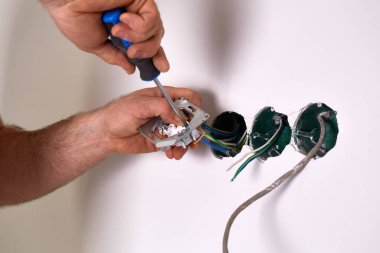 Bir işçi tornavida kullanarak duvara elektrik prizi takıyor..