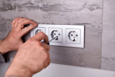 Bir elektrikçi porselen taşlarla kaplı bir duvara elektrik prizi takmak için tornavida kullanır..