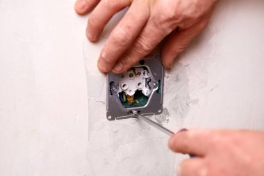 Bir işçi tornavida kullanarak duvara elektrik prizi takıyor. Daire tadilattan geçiyor..