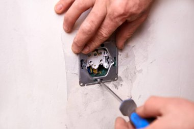 Bir işçi tornavida kullanarak duvara elektrik prizi takıyor. Daire tadilattan geçiyor..