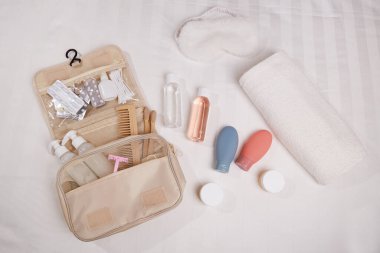Seyahat malzemeleri beyaz bir yüzeye düzgünce konur. Şişeler, kozmetik kavanozları, diş fırçaları, tarak ve havlu gibi temel kişisel hijyen malzemelerini içerir.