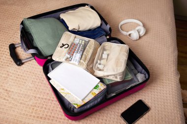 Açık bir bavul. İçinde kozmetik ürünleri, hijyen ürünleri, giysiler ve yatakta yolculuk için gerekli diğer şeyler var.