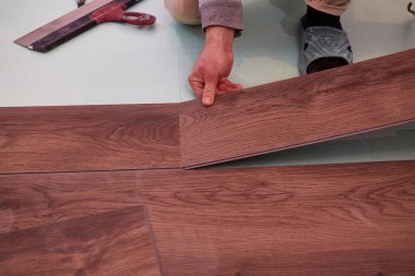 Bir işçi, pürüzsüz bir alt katman yüzeyine ev geliştirme projesinin bir parçası olarak lamine döşeme döşeme döşemesi serer.