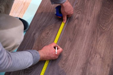 Bir işçi, kuvars vinil fayansın uzunluğunu ölçmek için mezura kullanır. Pürüzsüz bir alt katman üzerine bir ev geliştirme projesinin parçası olarak laminat veya kuvars vinil döşeme üzerinde çalışın.