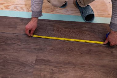 Bir işçi, kuvars vinil fayansın uzunluğunu ölçmek için mezura kullanır. Pürüzsüz bir alt katman üzerine bir ev geliştirme projesinin parçası olarak laminat veya kuvars vinil döşeme üzerinde çalışın.