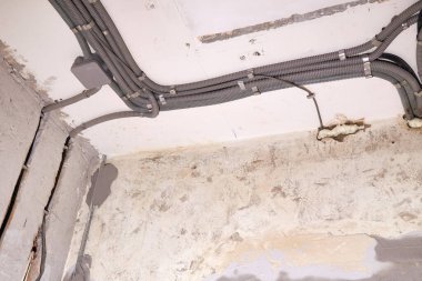 Koruyucu bir borunun içindeki elektrik kabloları ve tavana düzgün yerleştirilmiş bir dağıtım kutusu. Bir odaya yenilenen elektrik kablolarının kurulumu.